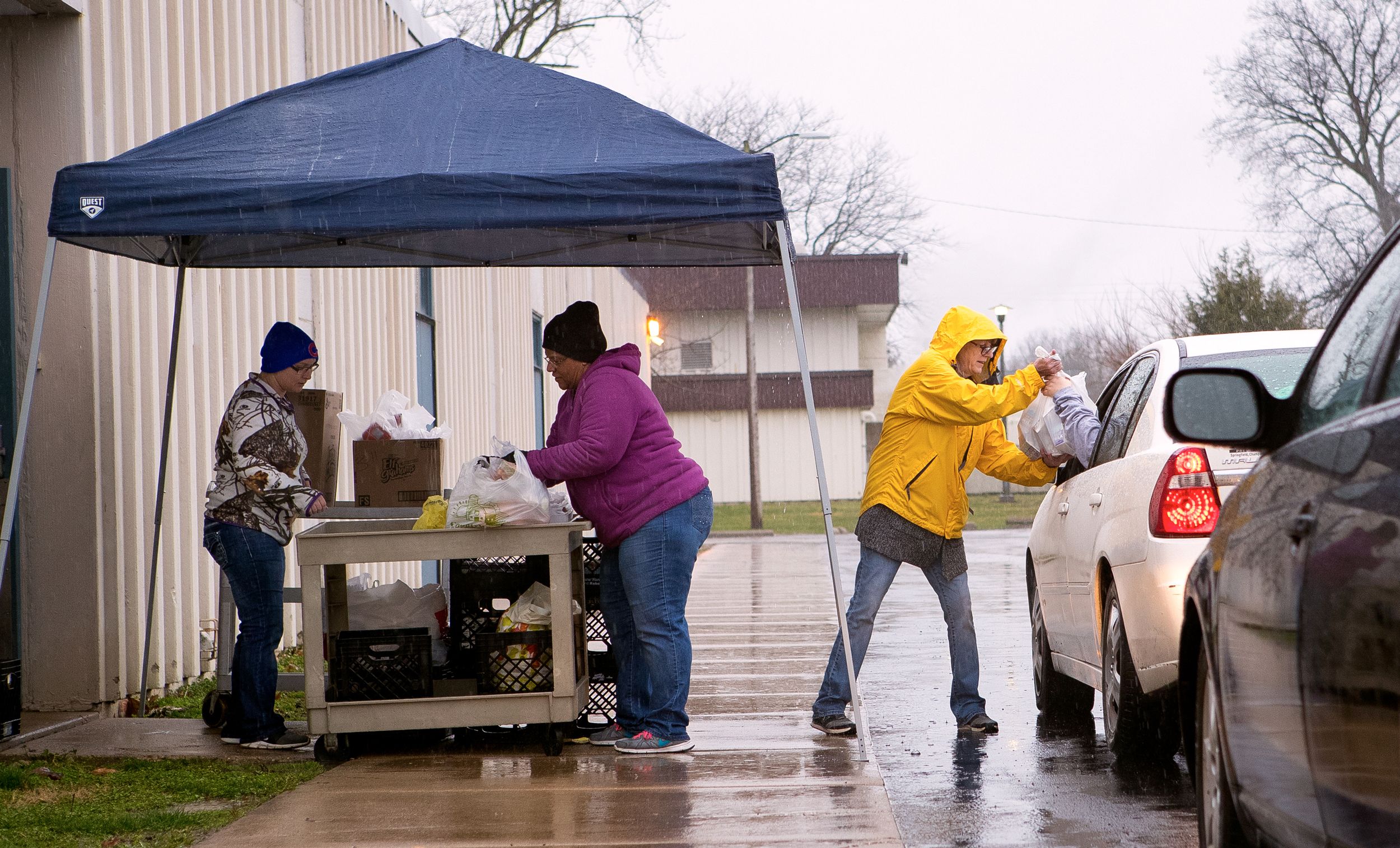 A canopy shelters volunteers from the rain while they distribute bagged meals to families in the parking lot at Southeast High School in Springfield, Illinois during COVID-19 school closure.