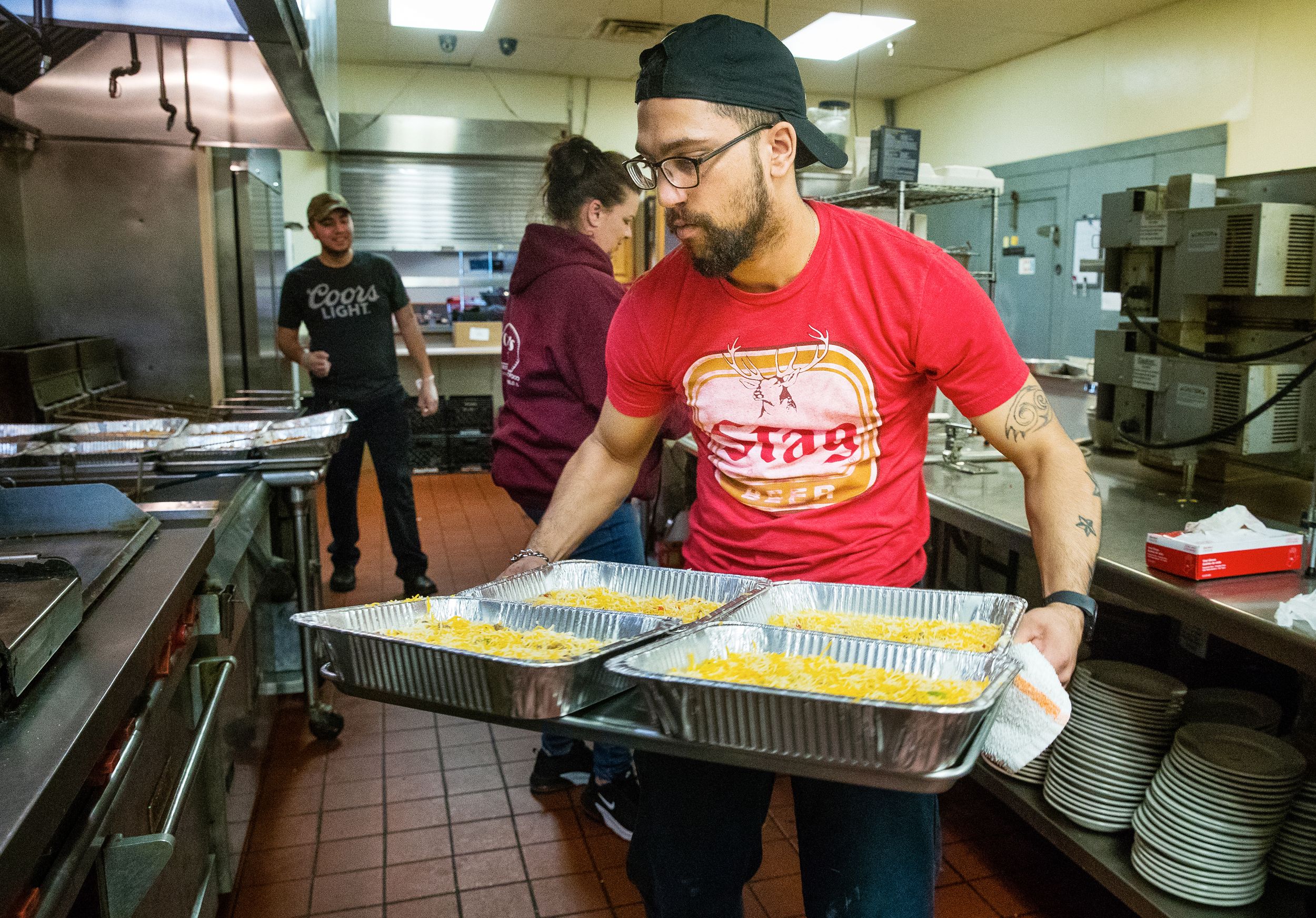 A man moves a large tray of food in an industrial kitchen.