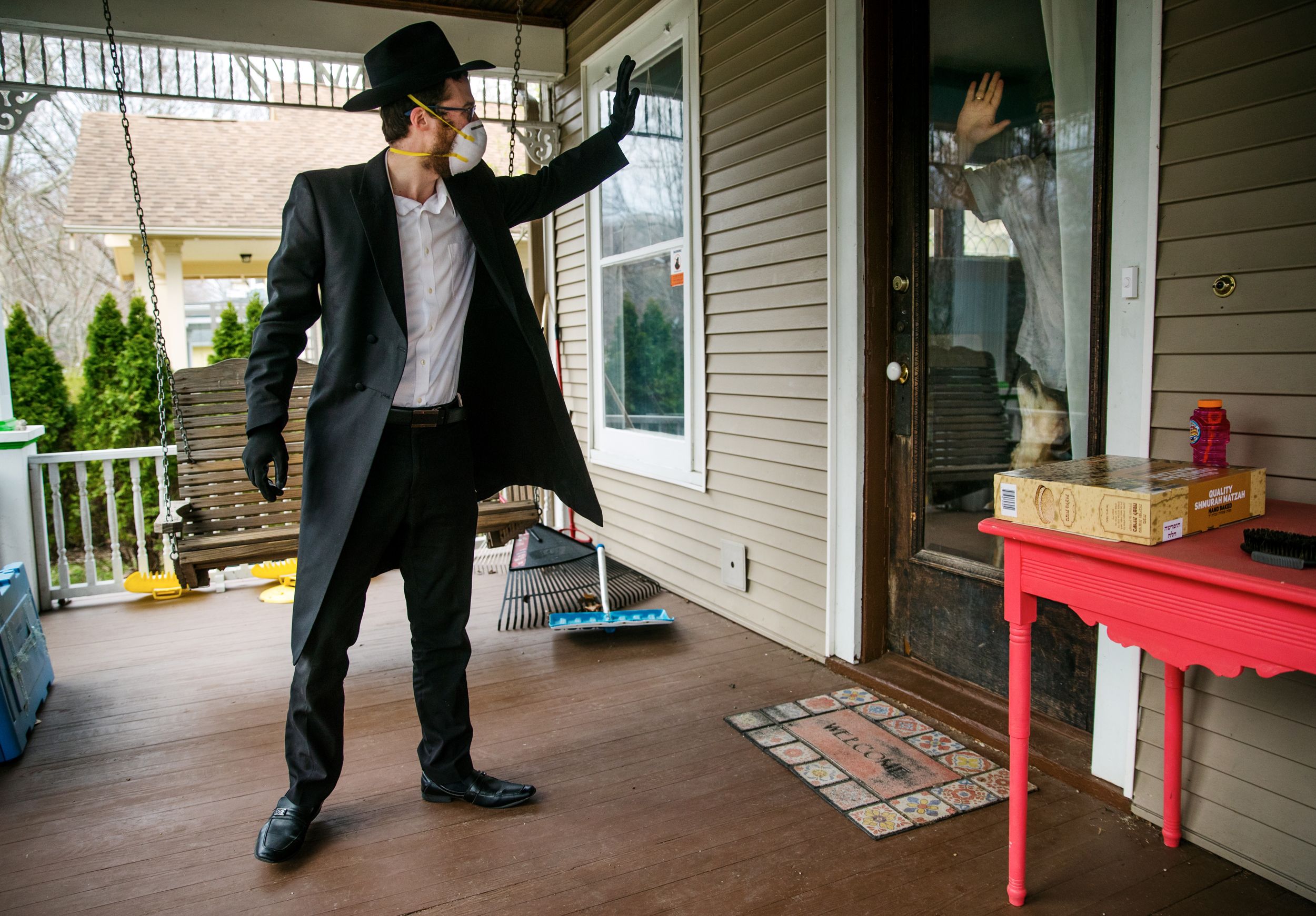 After leaving matzah on a table on the porch, a rabbi waves goodbye to Springfield family through glass door during COVID-19 pandemic, April 2020.