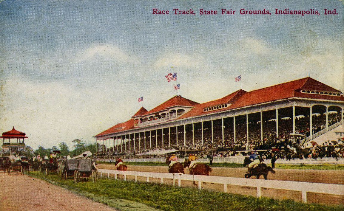 Illustrated postcard showing a horse race in front of grandstands at the Indiana State Fairgrounds racetrack around 1910. There are horse-drawn carriages on the infield watching the race but no cars are present.