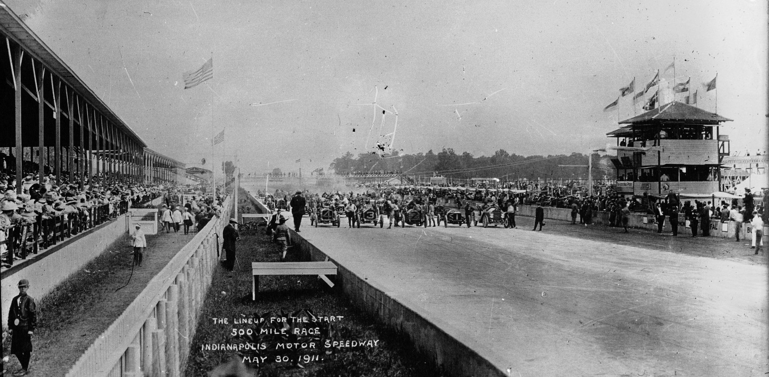 A historic photo from 1911 of race cars and a crowd of spectators before the International Sweepstakes at the Indianapolis Motor Speedway.