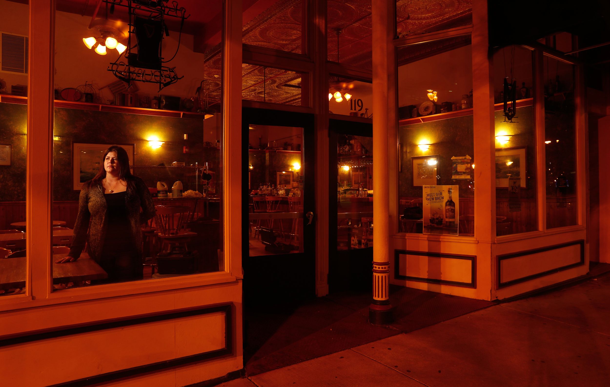 A female bartender stands in the window of a dark and empty bar in downtown Springfield.