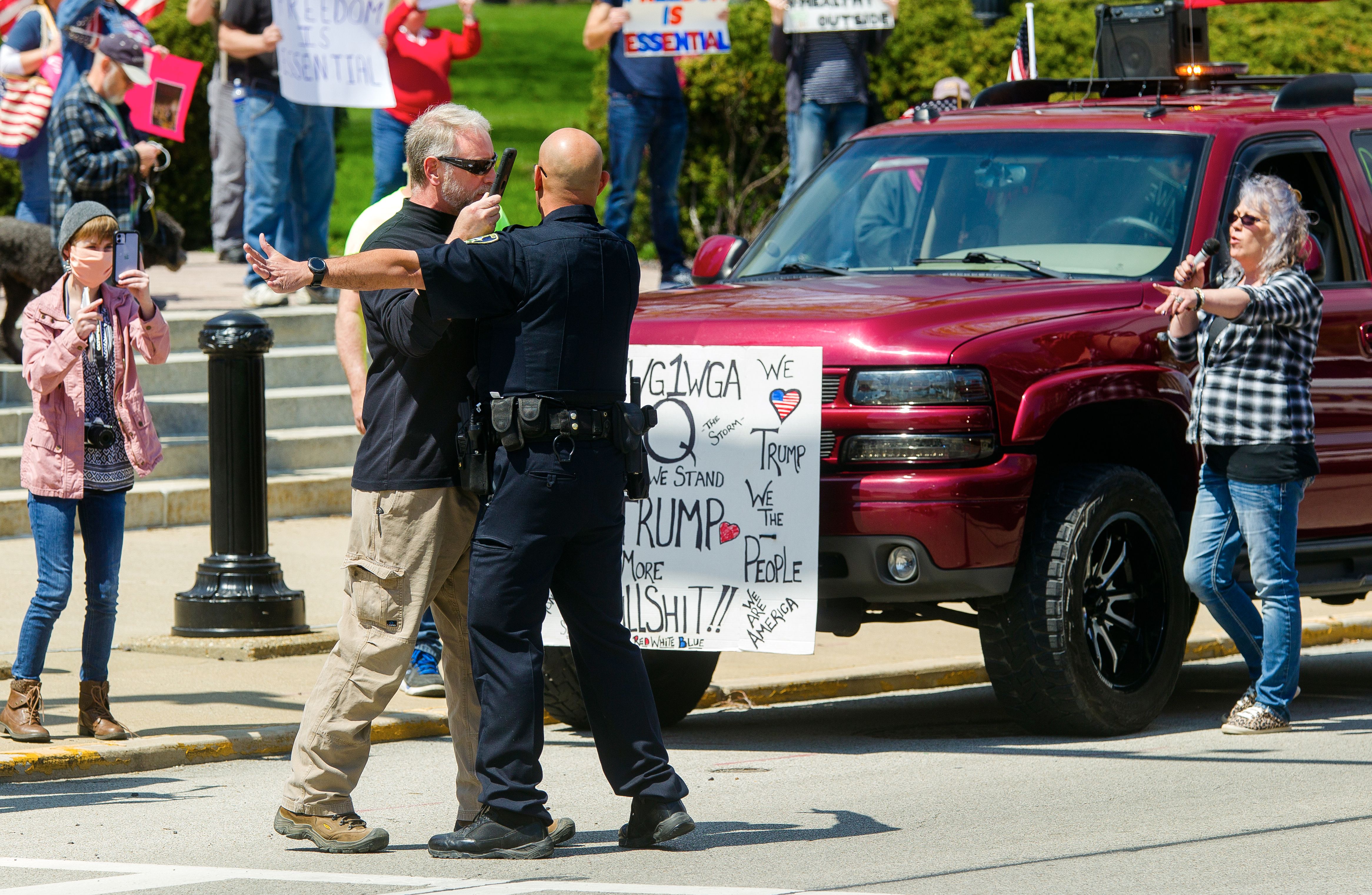 A Police officer directs protester who holds a phone directly in front of his face, off the street during a protest against COVID-19 policies at the Illinois Capitol, April 2020.