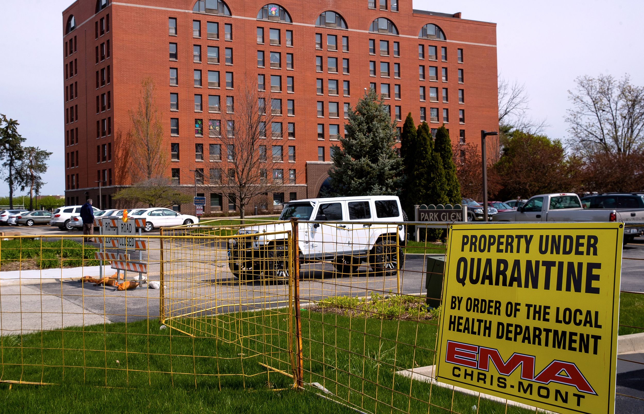 A yellow sign attached to temporary fence blocking access to a multistory red building in the background indicates 'PROPERTY UNDER QUARANTINE BY ORDER OF THE LOCAL HEALTH DEPARTMENT'.