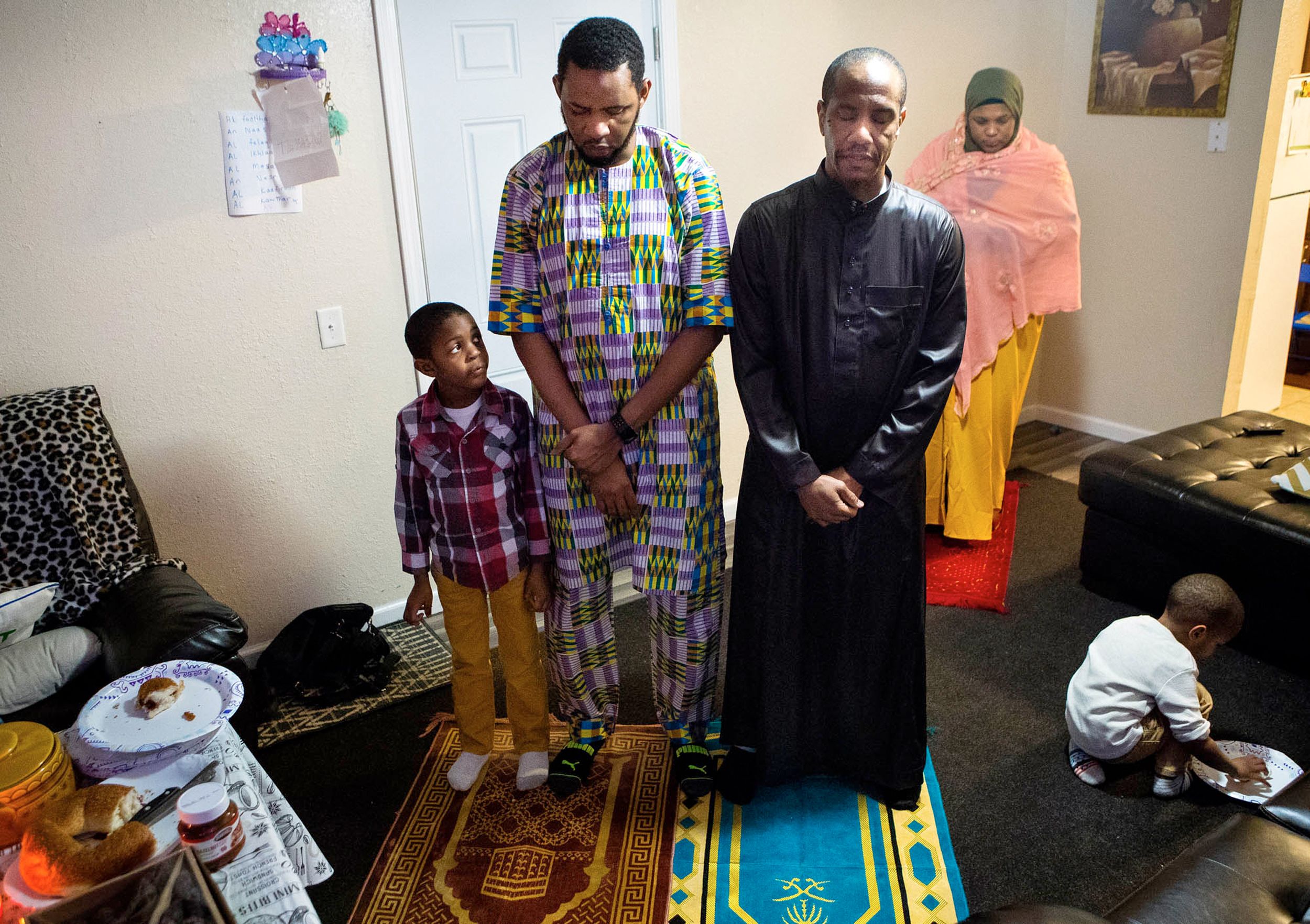 A small boy looks up at his father and uncle as they say their prayers during a Ramadan observance conducted in their apartment due to the COVID-19 stay-at-home orders.