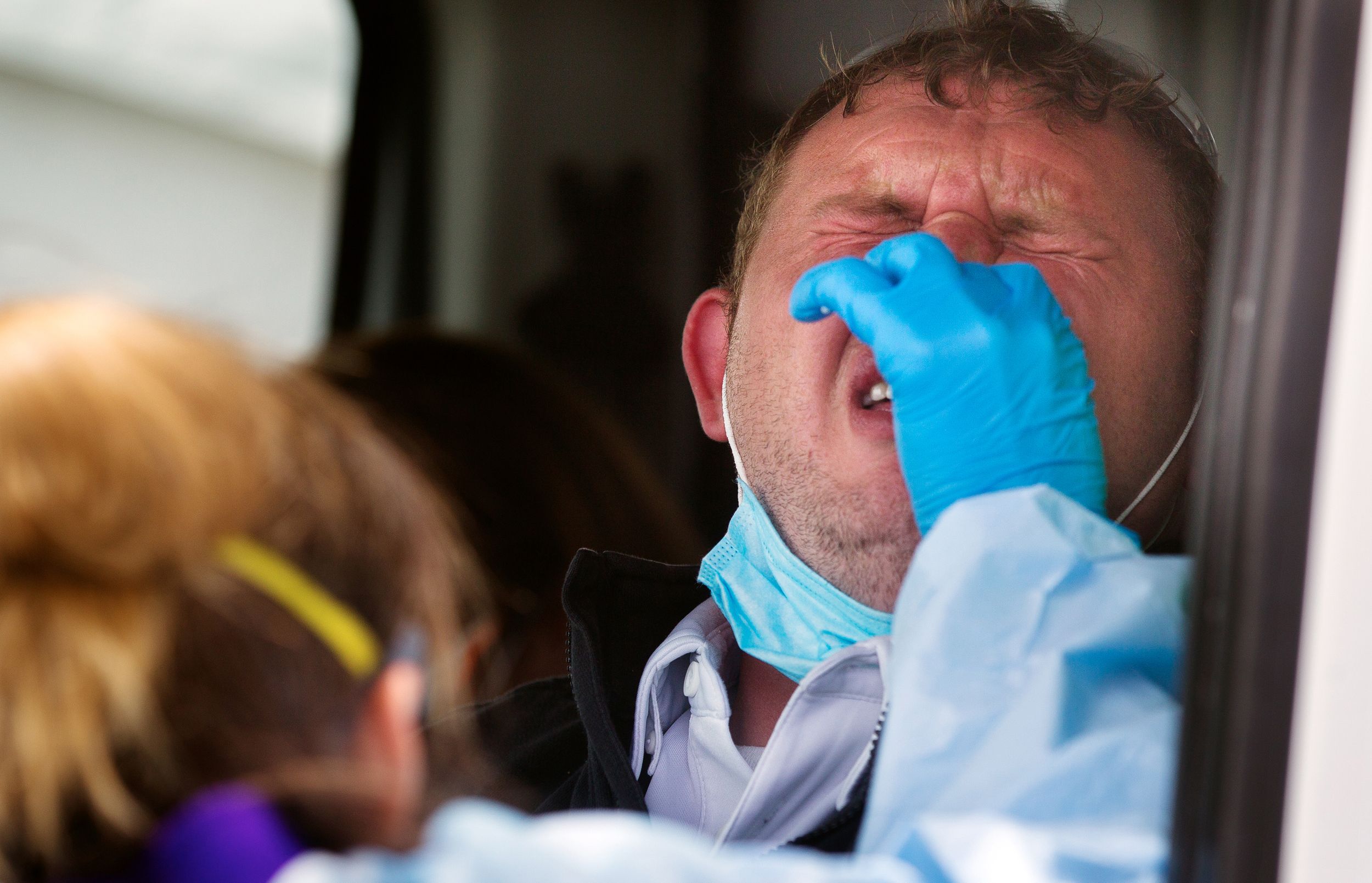 A man reacts as a medical worker administers a covid test with a nasal swab at drive-up covid testing site in May 2020.