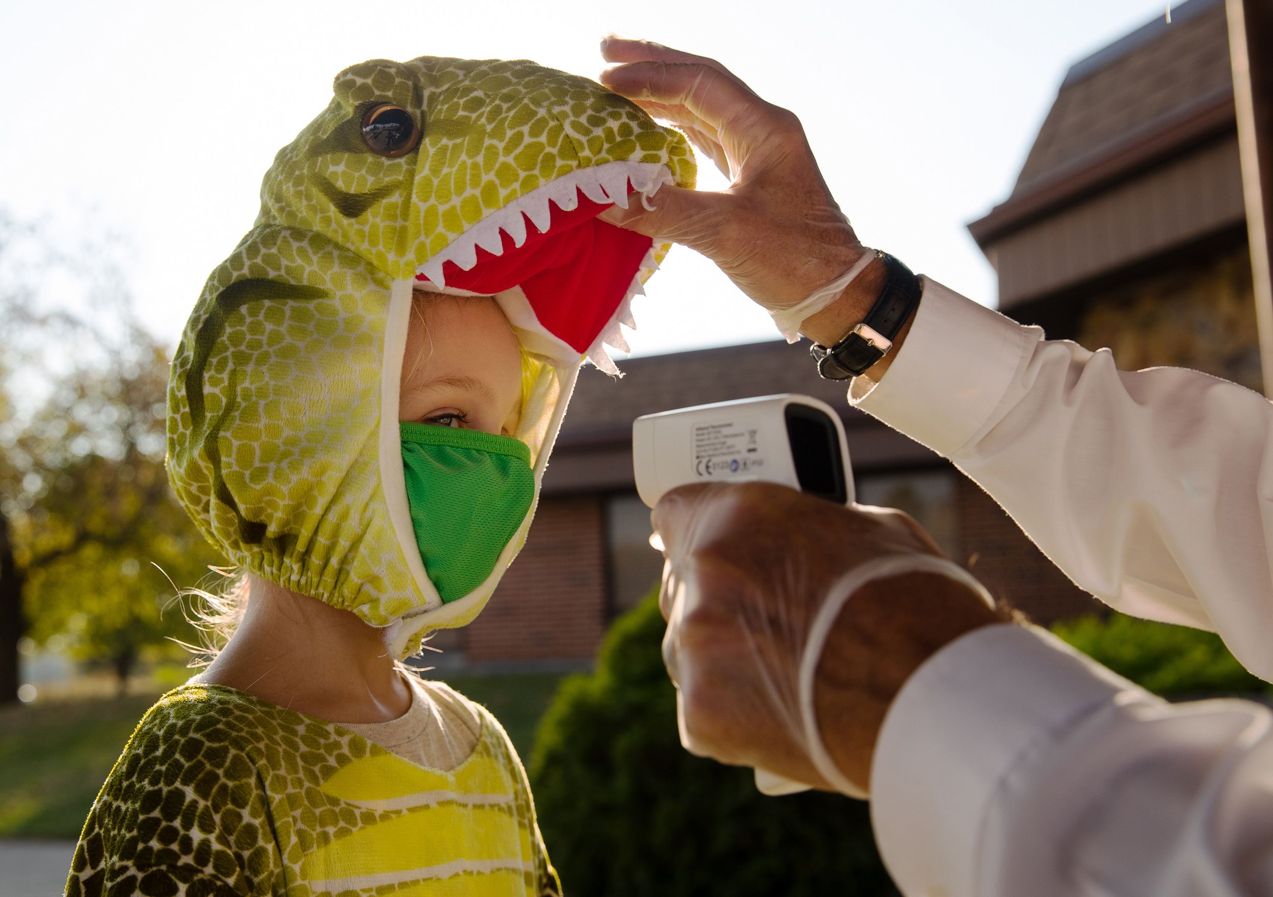 The mouth of a child’s dinosaur costume is lifted up so their temperature can be checked before their admittance to a Halloween event in October 2020.