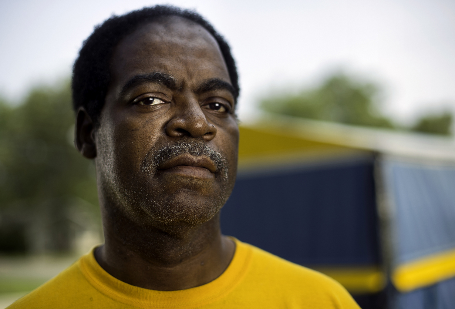 A man looks into the camera while standing in his yard.